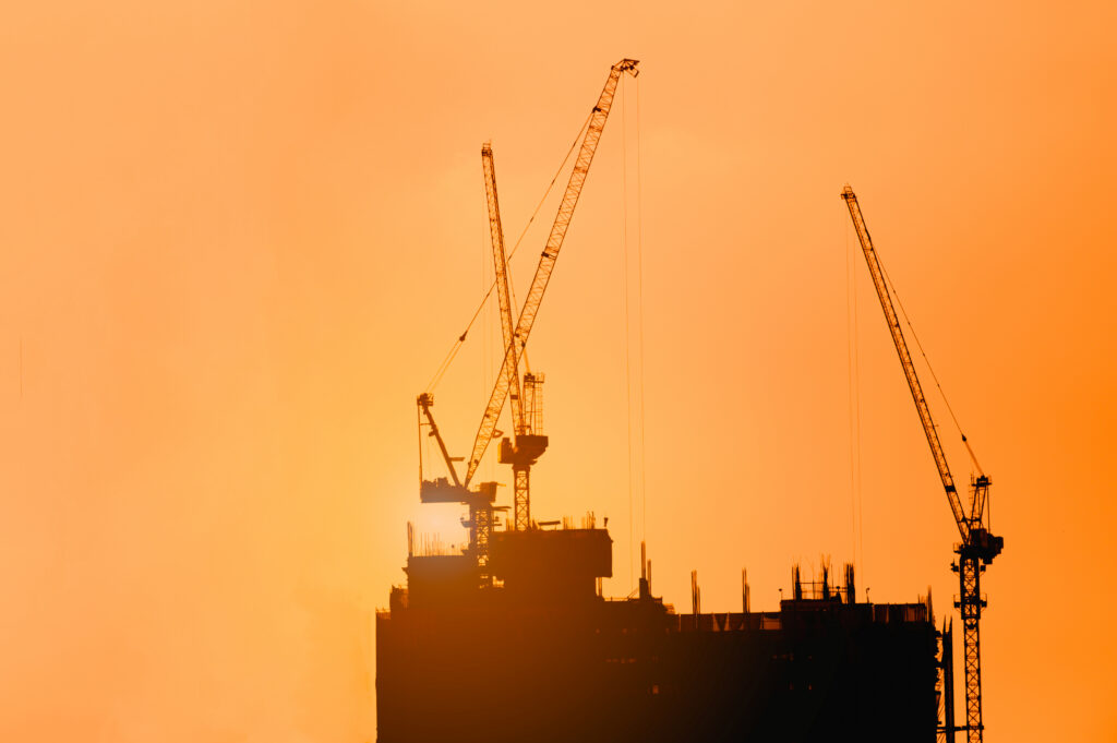 Construction cranes silhouetted against an orange sunset