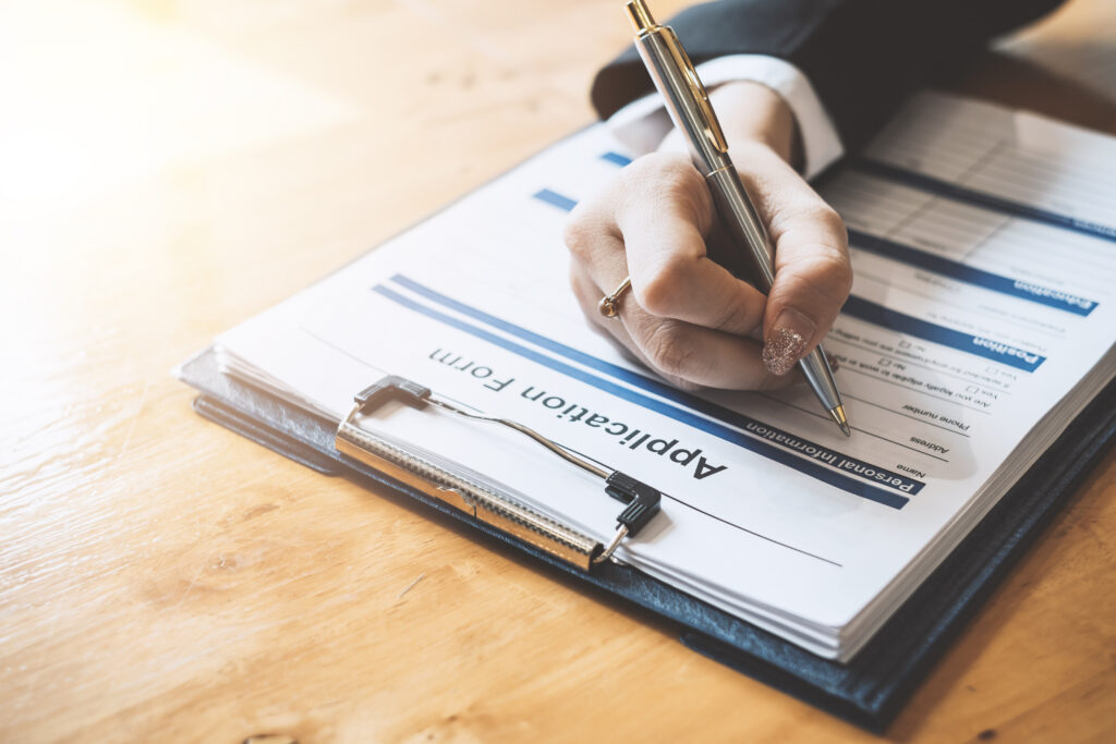 Person completing an application form on a clipboard