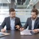 Business executives reviewing merger and acquisition agreements, financial documents, and transaction terms